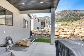 Et moderne hus med en overdækket terrasse, stenvægge og udsigt til bjerge.