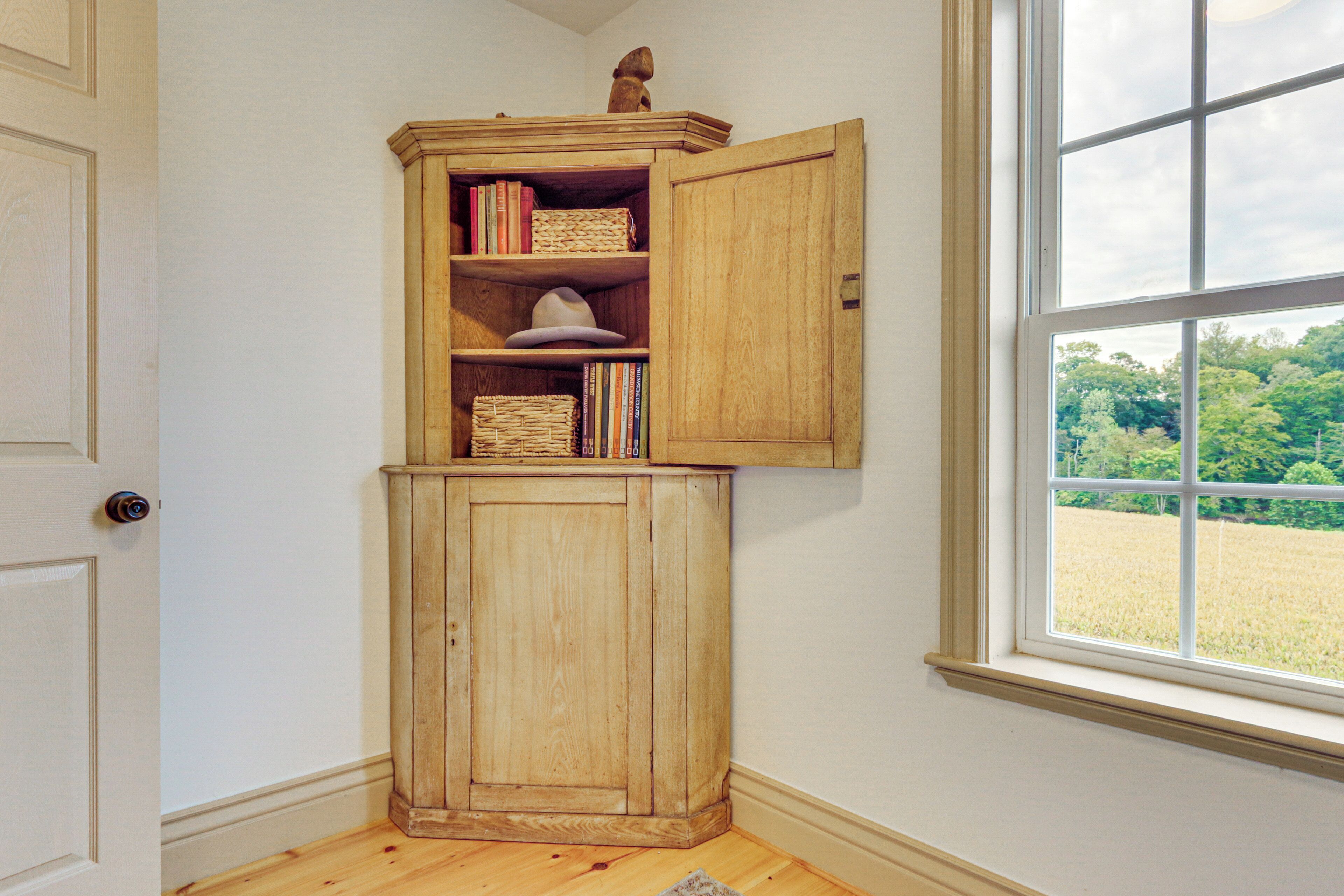 Una habitación de esquina con un armario de madera, una ventana que da a un campo y una puerta.