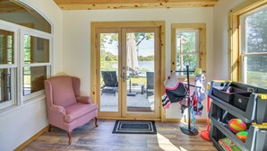 Une pièce avec un plafond en bois, un fauteuil rose, une porte-fenêtre coulissante donnant sur un espace extérieur et un présentoir rempli de jouets pour enfants.