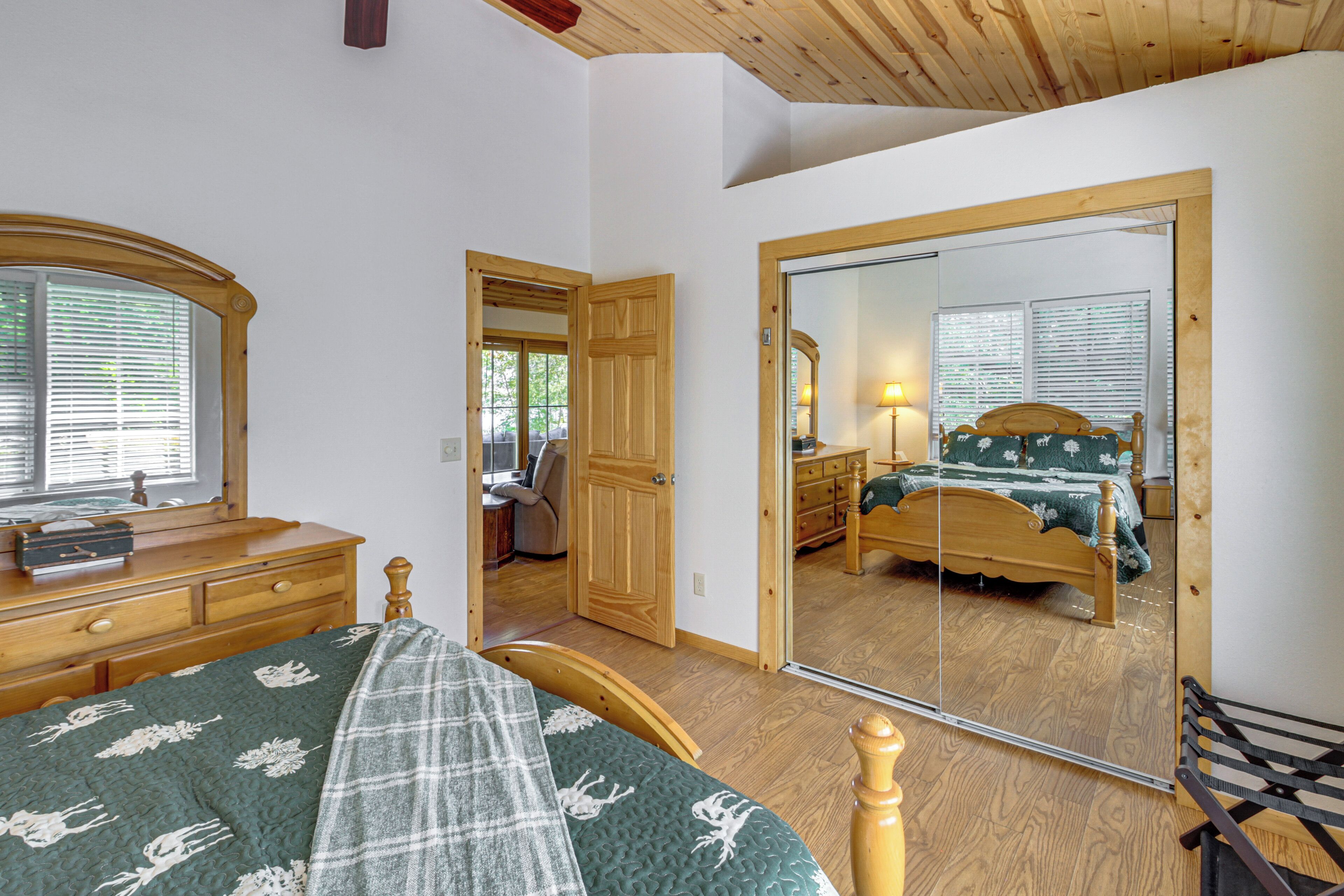 A bedroom with a bed, wooden dresser, and a large mirror reflecting another room.