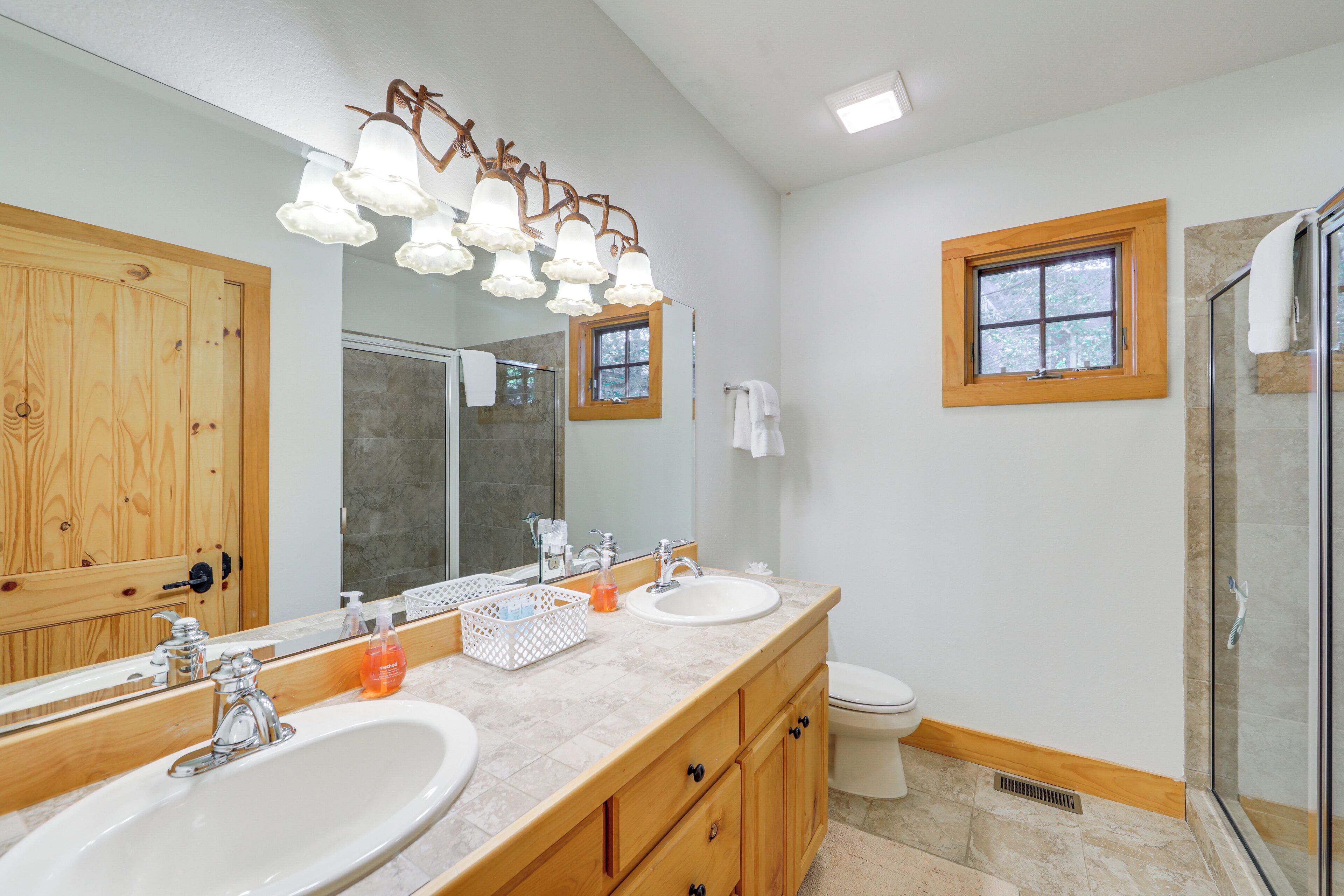 A bathroom with a wooden vanity, two sinks, a large mirror, a shower with glass doors, and a window.