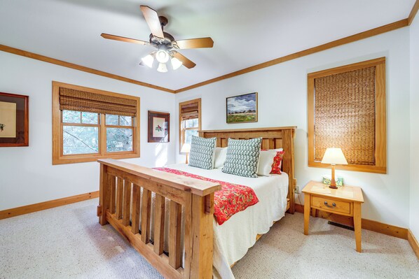 A bedroom with a wooden bed, a nightstand, a ceiling fan, and a large window with blinds. - Scenic Mtn & Fairway Views: Cozy Cashiers Getaway (Cashiers)