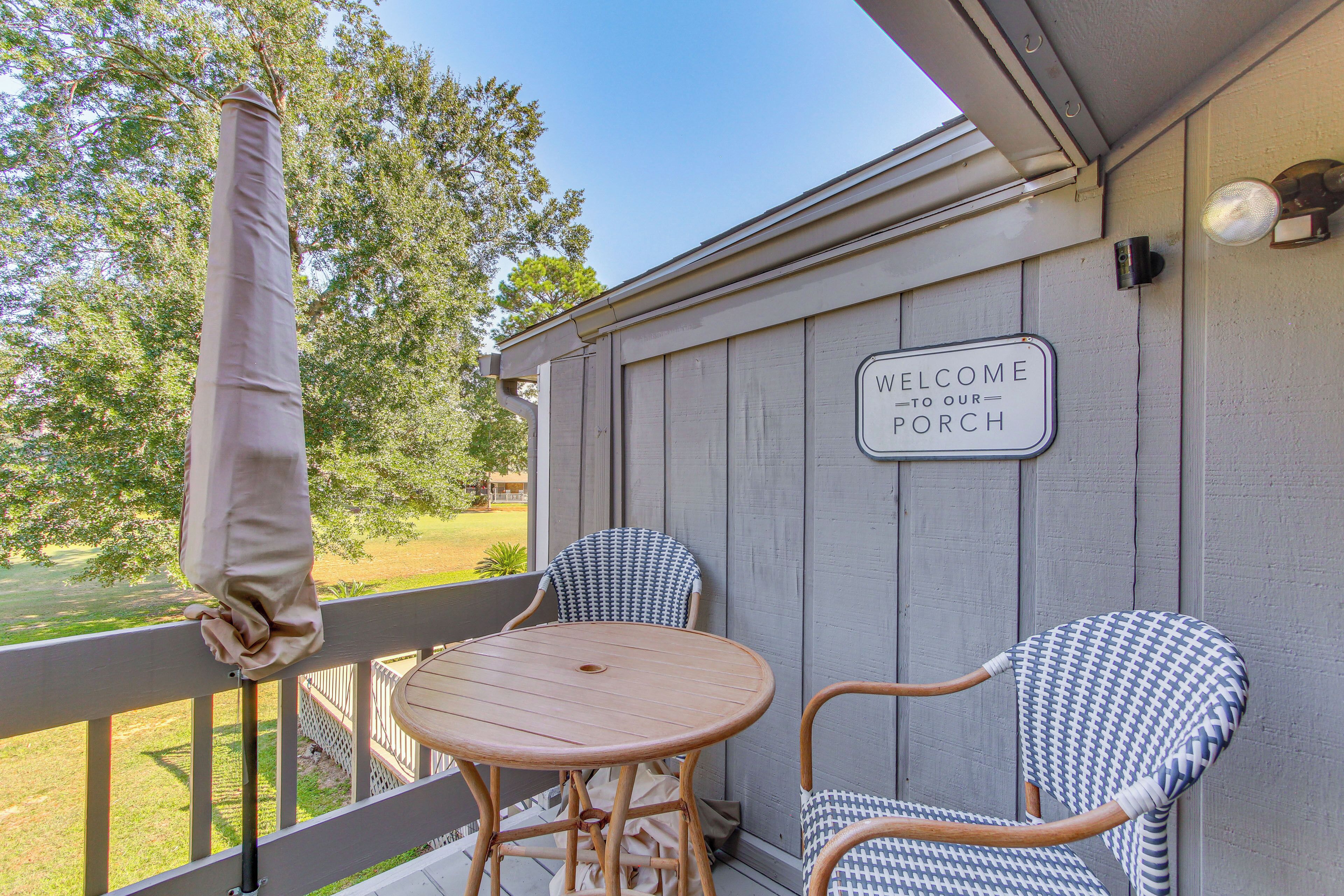 A porch with two wicker chairs and a wooden table, a 'Welcome to our Porch' sign, and a view of a green landscape.
