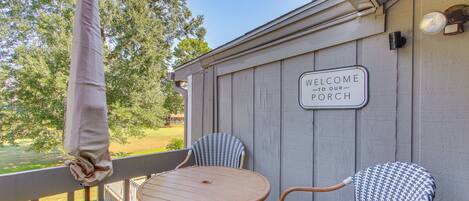 A porch with two wicker chairs and a wooden table, a 'Welcome to our Porch' sign, and a view of a green landscape.