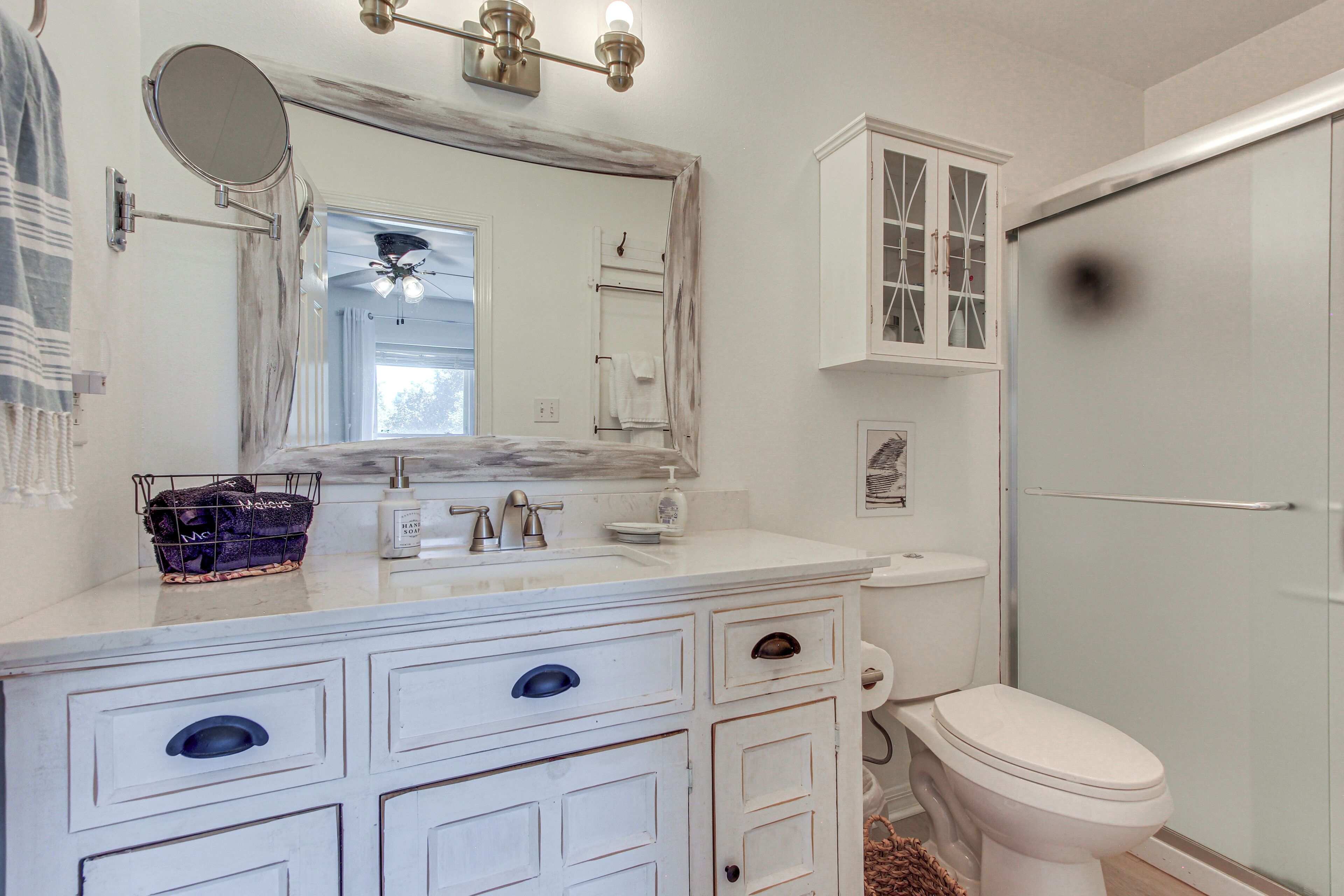 A bathroom with a white vanity, a mirror, a towel rack, a toilet, and a shower area.