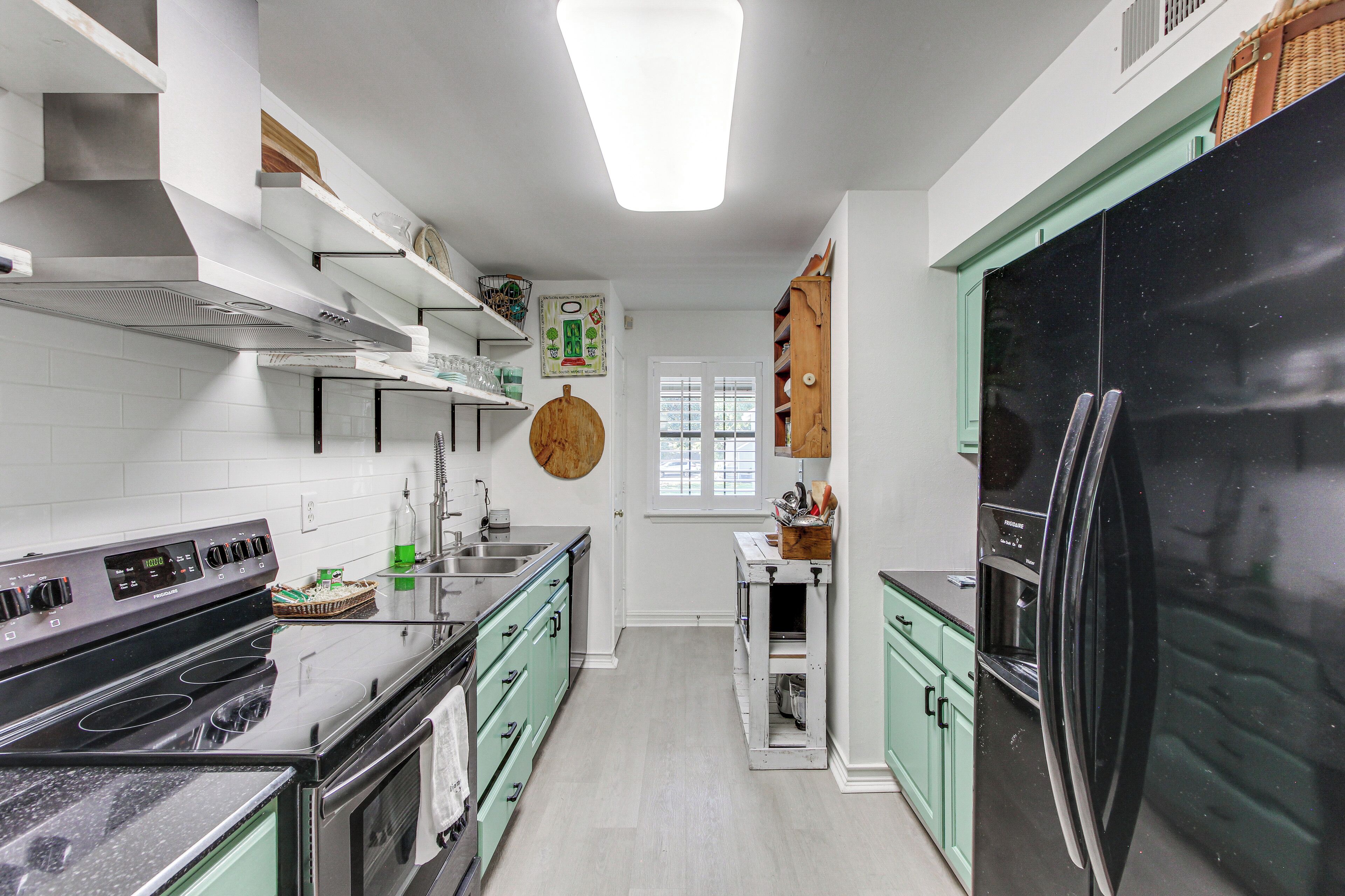 Une cuisine moderne avec un réfrigérateur noir, des appareils en acier inoxydable et des meubles de couleur vert clair.