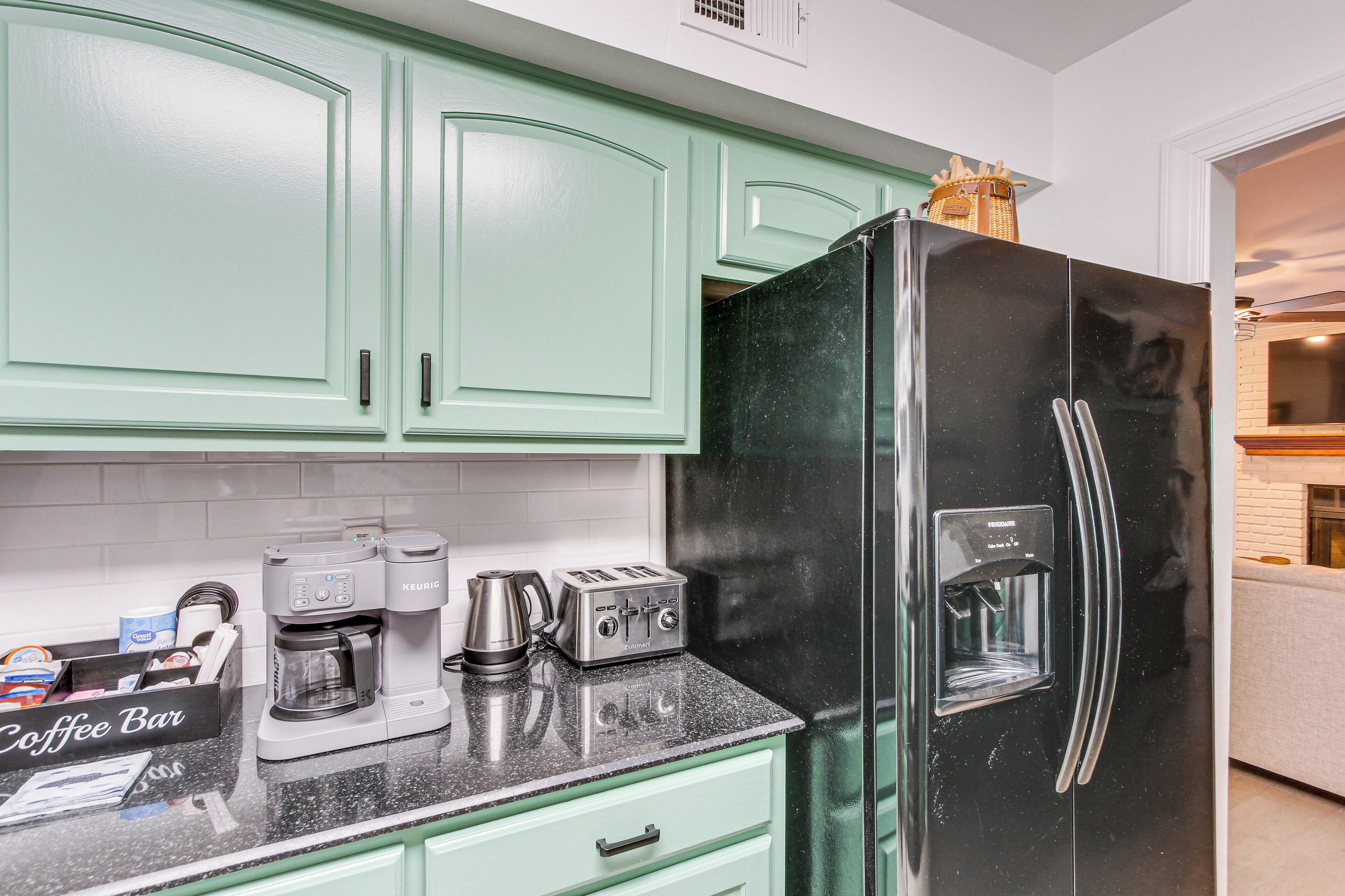 A kitchen with teal cabinets, a black refrigerator, a coffee maker, and a toaster.