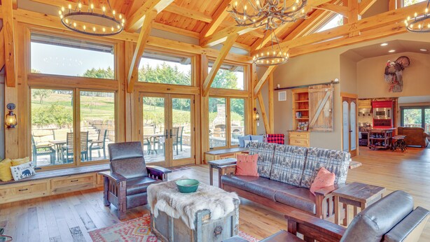 A spacious living area with a wooden ceiling, large windows, and a cozy seating arrangement. - Stay & Sip: Group Ranch at Shamrock Hills Vineyard (Excelsior Springs)