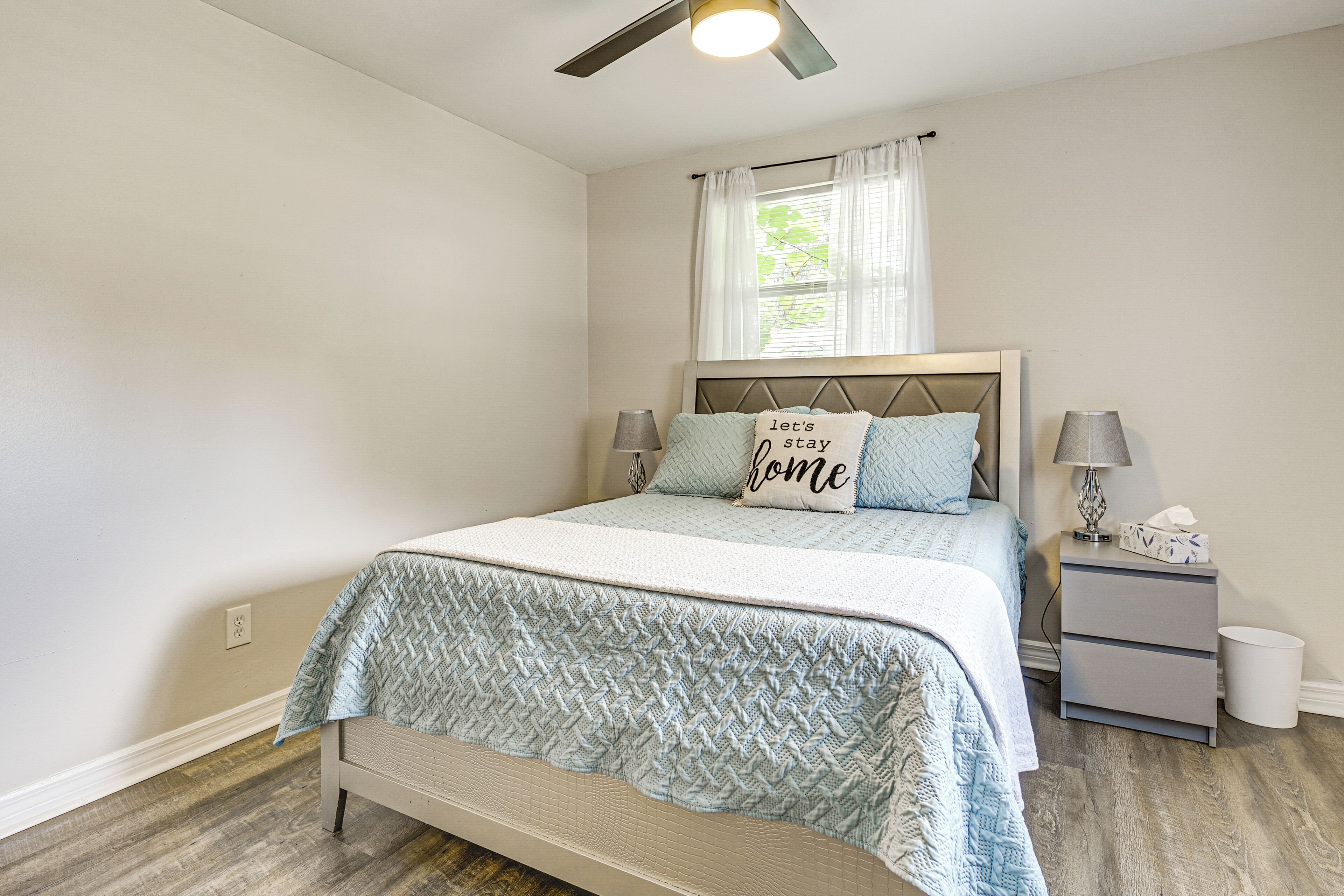 A bedroom with a bed, a nightstand, a lamp, a ceiling fan, and a window with curtains.
