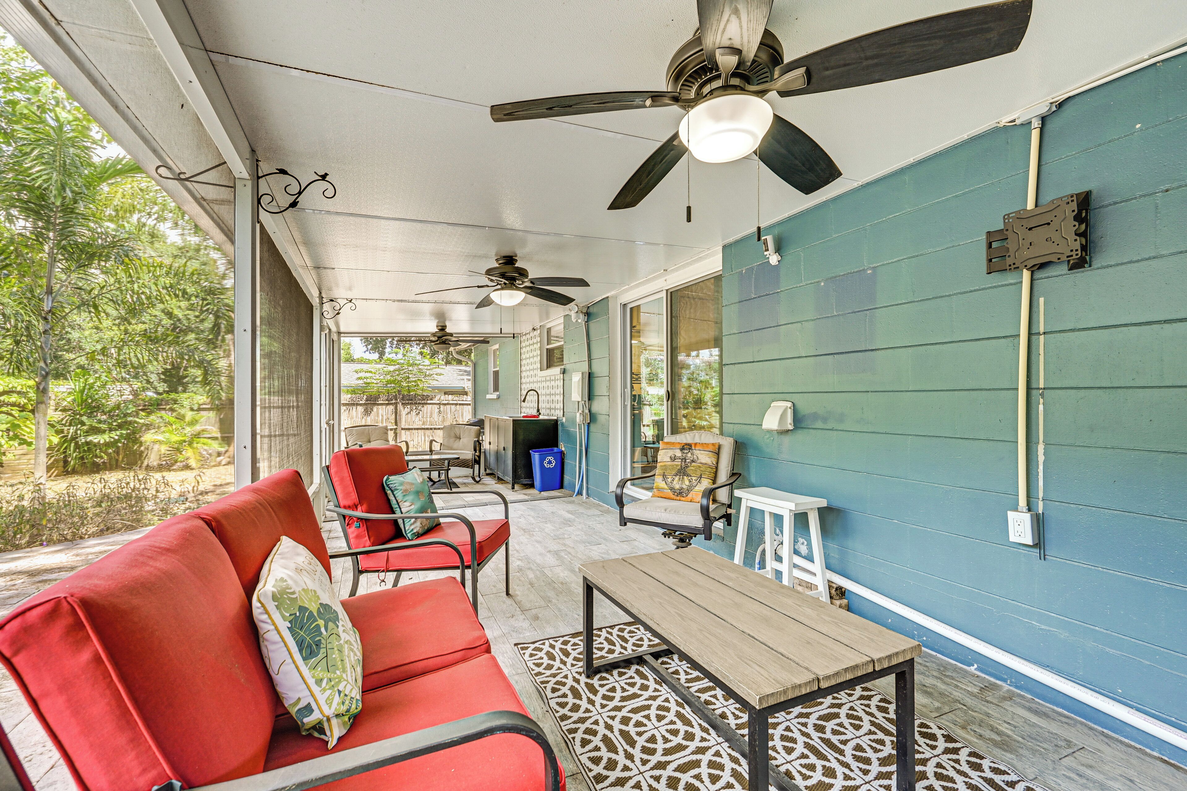 A covered outdoor area with a red sofa, two chairs, a wooden table, and ceiling fans.