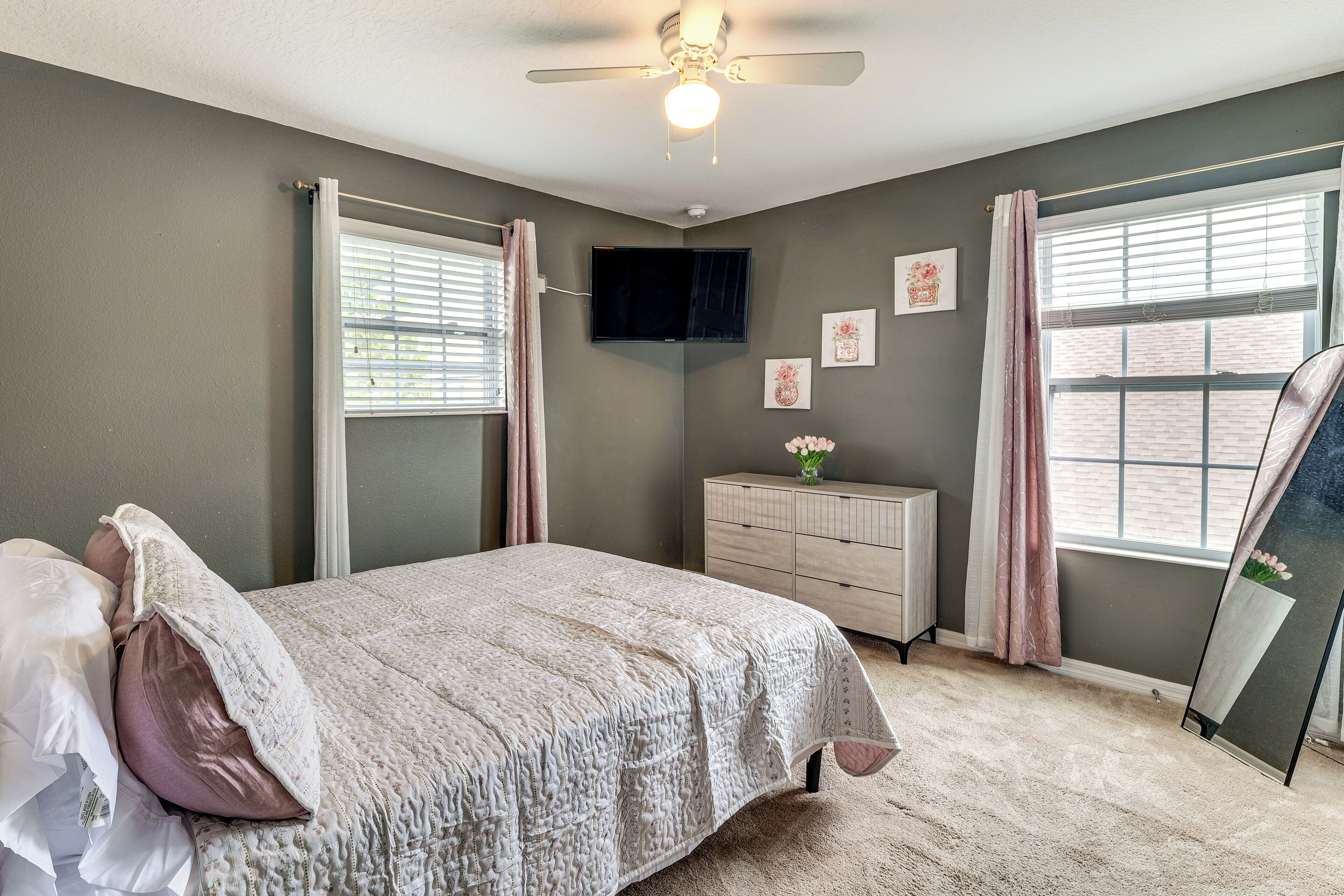 A bedroom with a bed, a dresser, a mirror, and a ceiling fan.