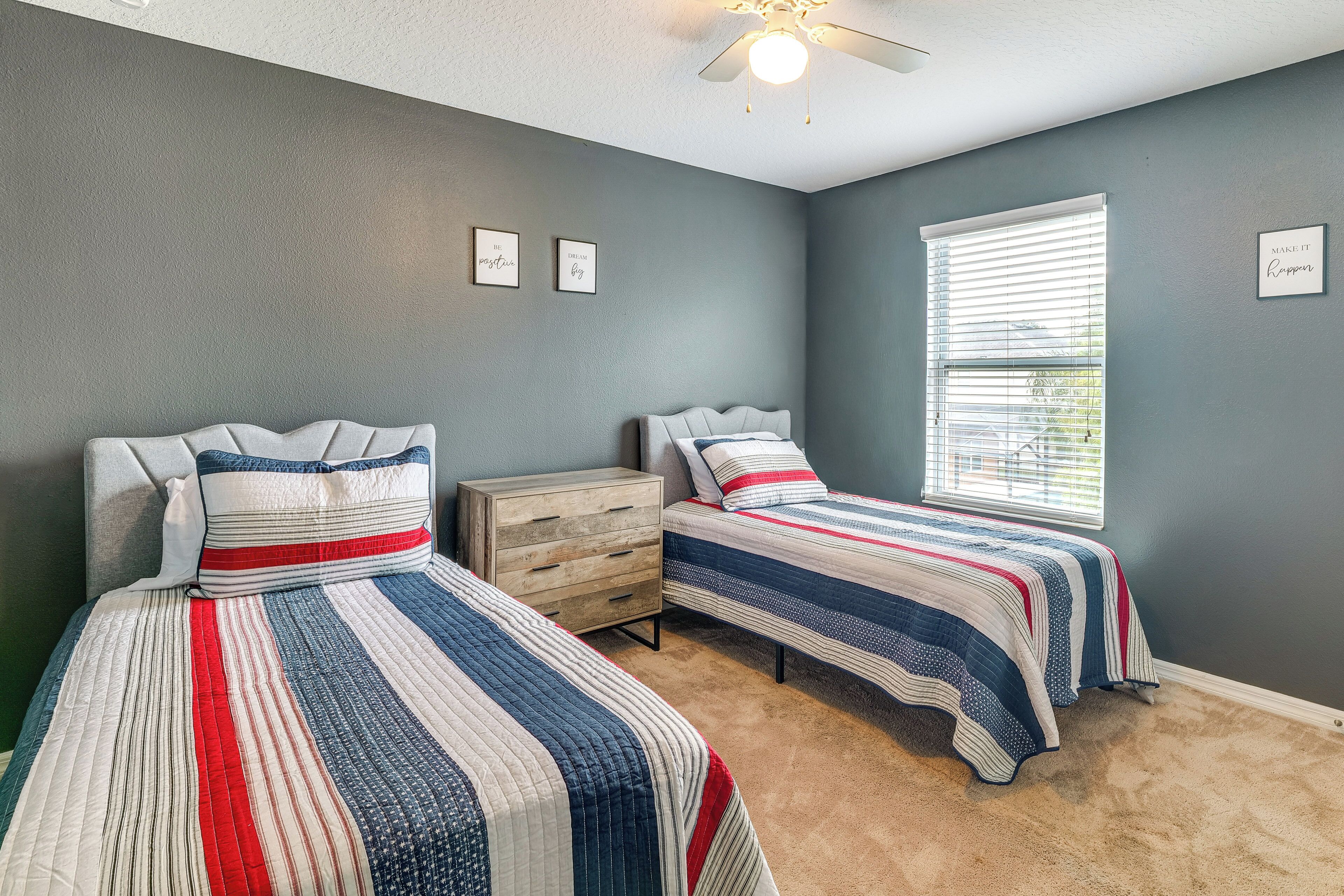 A bedroom with two beds, a ceiling fan, and a window with blinds.