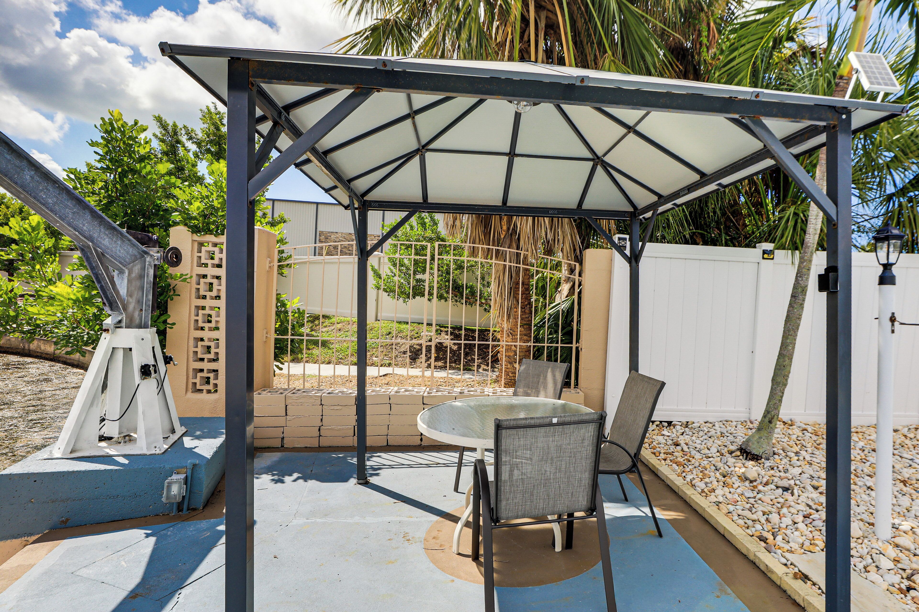 A covered patio area with a table and chairs, a telescope, and a white fence in the background.