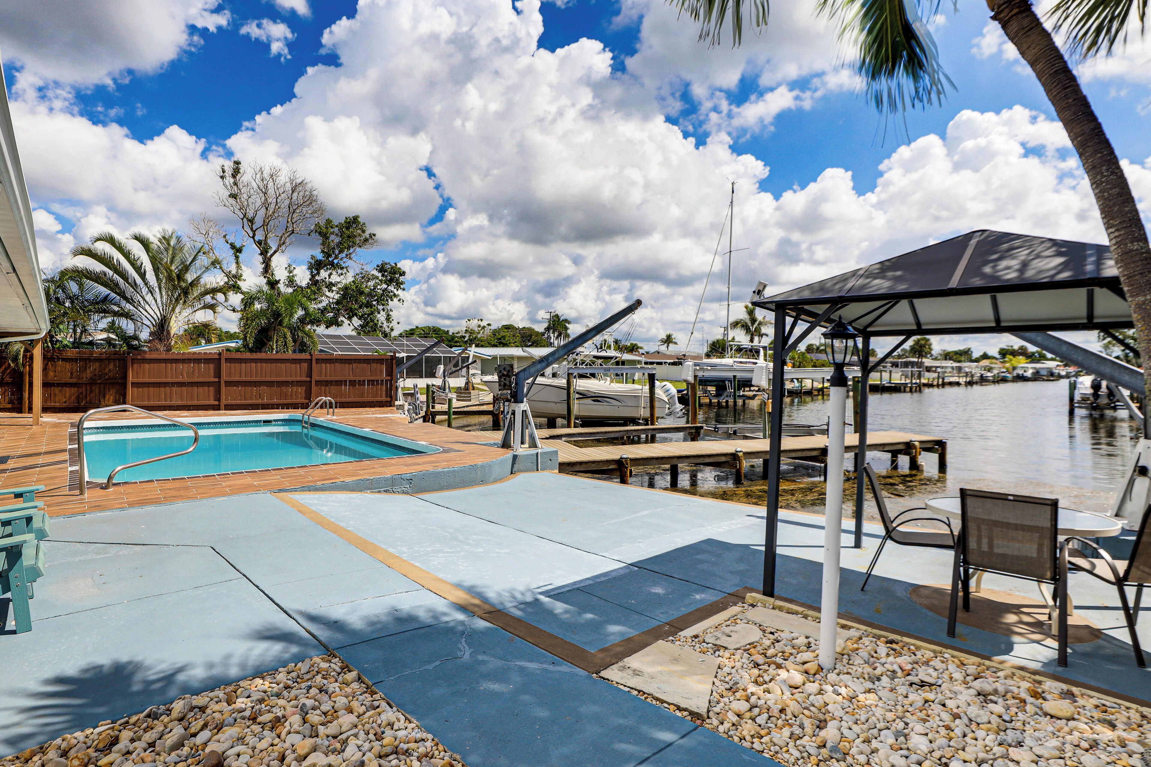 A pool area with a wooden deck, a covered seating area, and a view of the water.