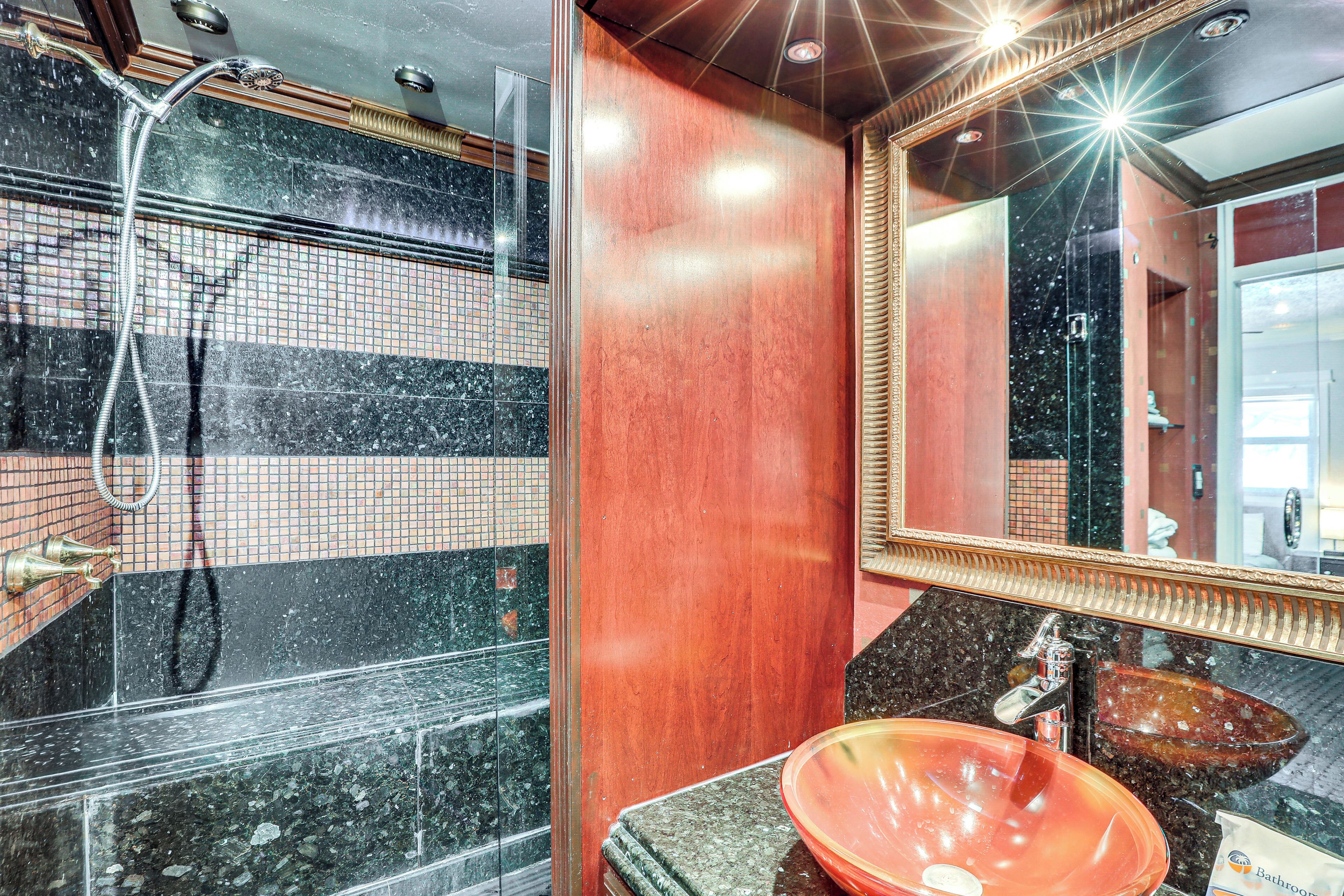 Une salle de bain dotée d’une douche à parois de verre, d’un mur recouvert de carreaux de marbre, d’un meuble-lavabo en bois et d’un grand miroir.