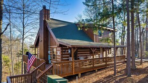 Eine Holzhütte mit einer Holzterrasse, einer Treppe und Blick auf den umliegenden Wald.