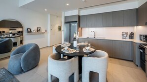 A modern kitchen with grey cabinets, a dining area with a round table and grey chairs, and a visible island with a sink. - Iconic Burj Khalifa & Fountain Views, 2BR Downtown (Dubai)