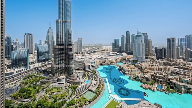 A high-rise building with a distinctive curved design, surrounded by a cityscape with various other skyscrapers. - Iconic Burj Khalifa & Fountain Views, 2BR Downtown (Dubai)
