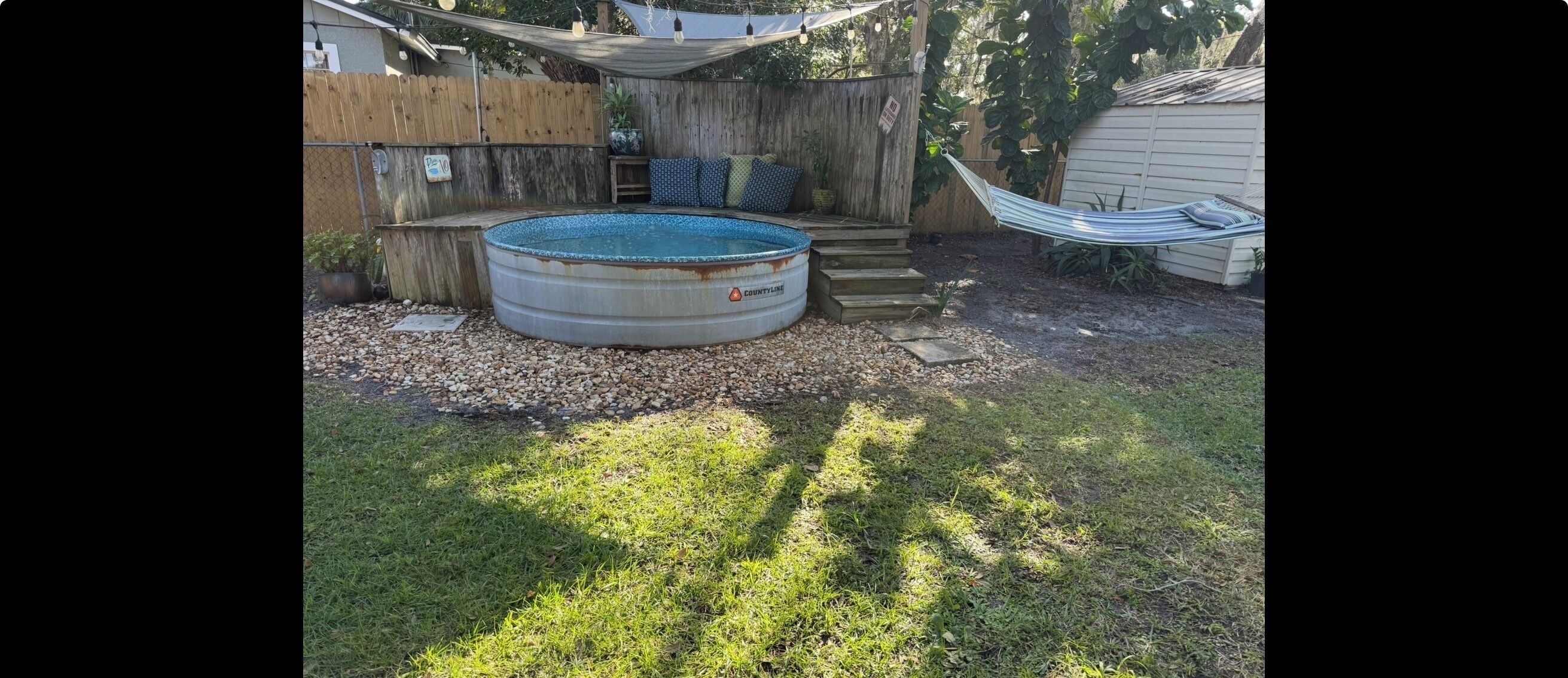 Um quintal com piscina enterrada redonda, uma rede e um deck de madeira.