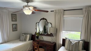 A hotel room with two single beds, a desk with a chair, a large mirror, and a ceiling fan.