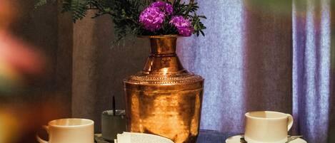 A table with a copper vase, two cups, and an open book.