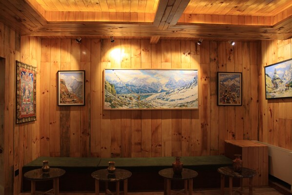 Una habitación con paneles de madera, un cuadro grande de un paisaje montañoso, un banco verde y pequeñas mesas redondas con velas.