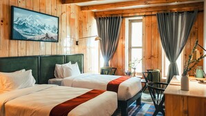 A hotel room with two beds, a desk, a chair, and a window with curtains.
