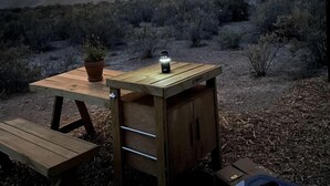 Un'area campeggio all'aperto con un tavolo, una lanterna e un armadietto portatile sotto una tenda da sole.