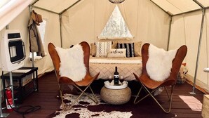 Una tenda con due poltrone in pelle, un tavolino con una bottiglia e dei bicchieri, e un tappeto in pelle di mucca.