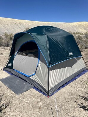 A dome-shaped tent with a gray and blue color scheme, set on a rocky ground with sparse vegetation in the background. - Serene Glamping Tent Incredible to Relax and Disconnect in Delta, Colorado (Delta)