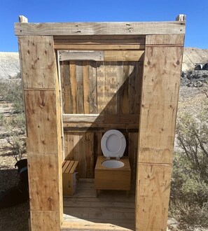 Eine hölzerne Außentoilette mit WC und einer kleinen Bank.