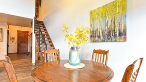 Un coin repas comprenant une table ronde en bois, quatre chaises en bois et un vase avec des fleurs jaunes.