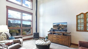 Un salon doté d’une grande fenêtre, d’une cheminée, d’un téléviseur et d’un meuble en bois.