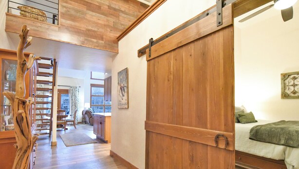 Un intérieur en bois avec une porte coulissante de style grange, un escalier et un lit recouvert d’une couverture verte.