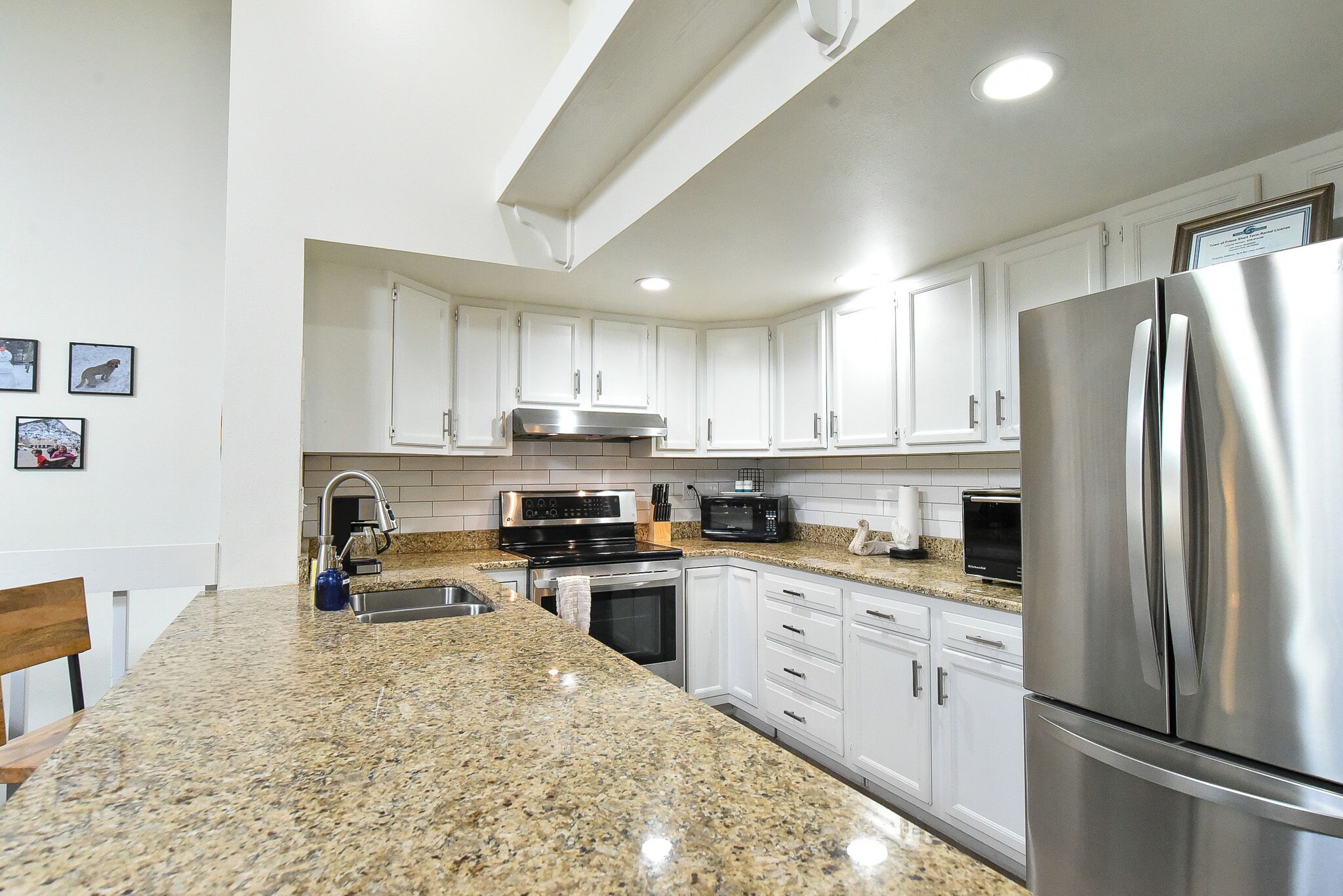 A modern kitchen with white cabinets, granite countertops, stainless steel appliances, and a built-in oven.