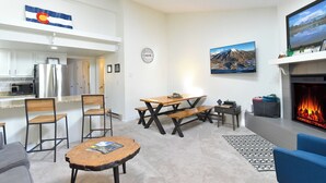 Ein modernes Wohnzimmer mit Kamin, einem Essbereich und einer durch eine offene Tür einsehbarer Küche.