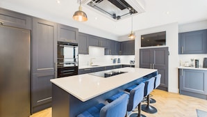 Cocina moderna con armarios grises oscuros, una isla grande con taburetes de bar, electrodomésticos de acero inoxidable e iluminación colgante.