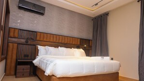 A modern bedroom with a wooden headboard, a flat-screen TV mounted above the bed, and a bedside table with a drawer. - Grayville Hotels and Bistro (Akure)