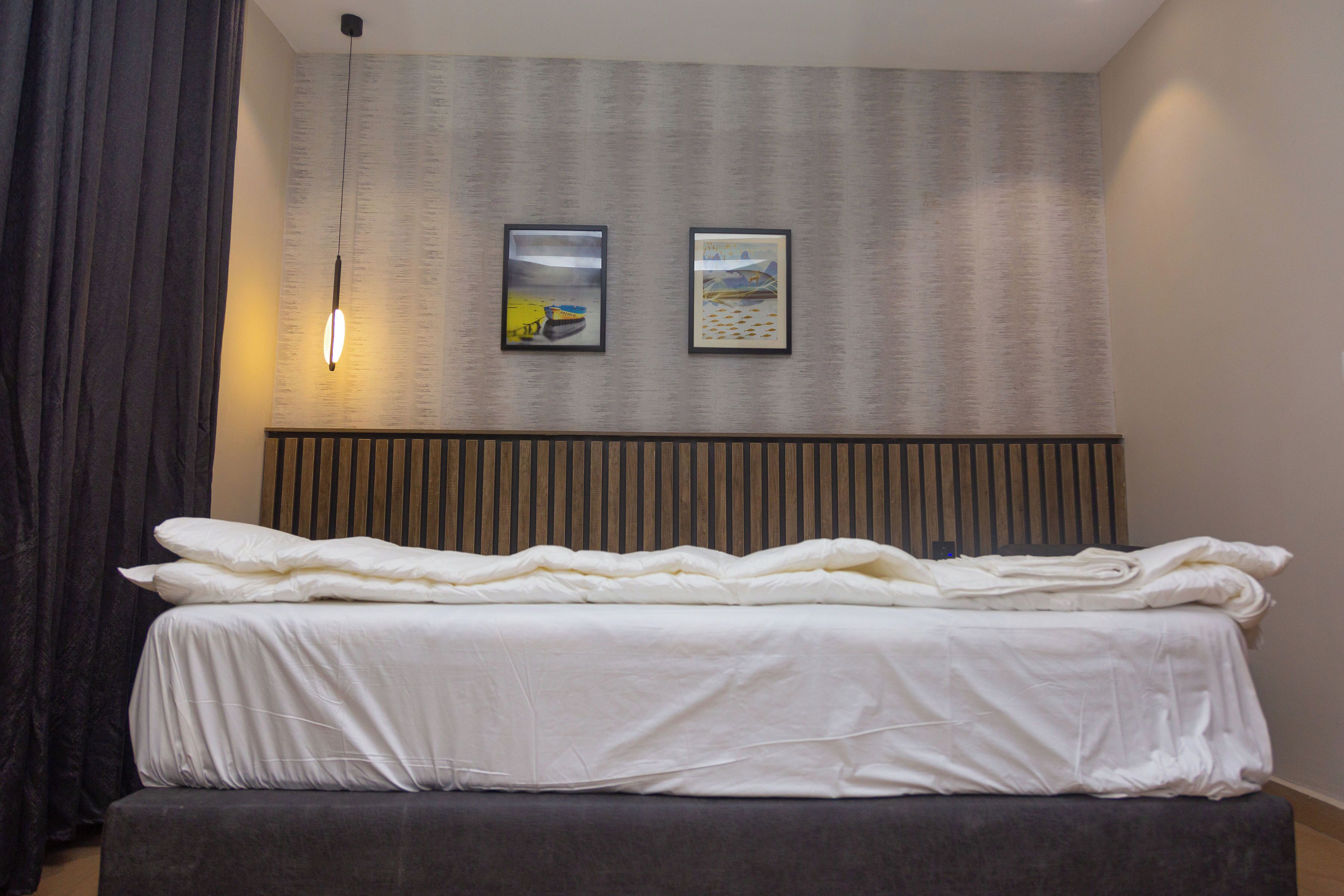A neatly made bed with white bedding, a headboard with vertical slats, and two framed pictures on the wall.