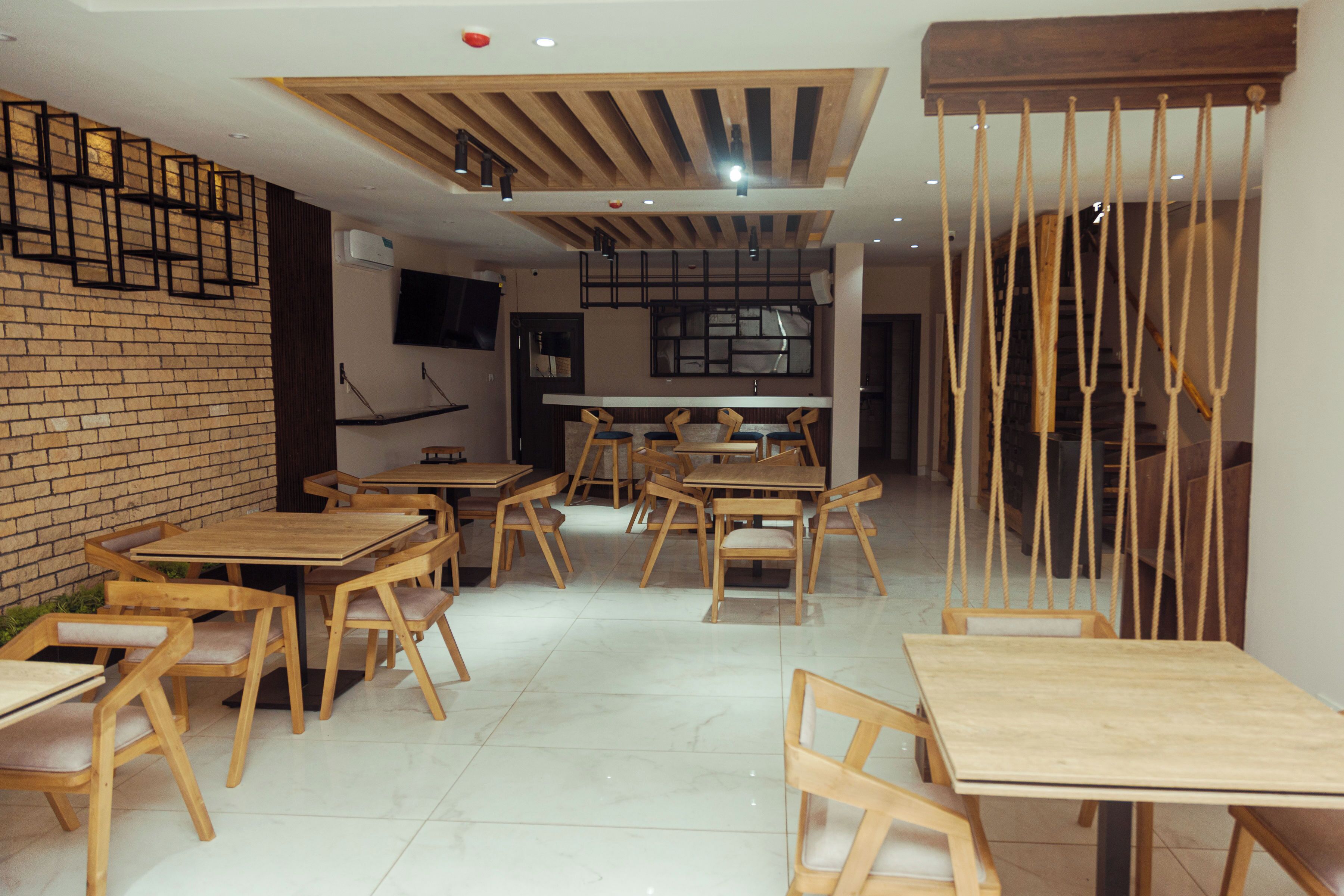 A restaurant interior with wooden tables and chairs, a brick wall, and a modern ceiling design.