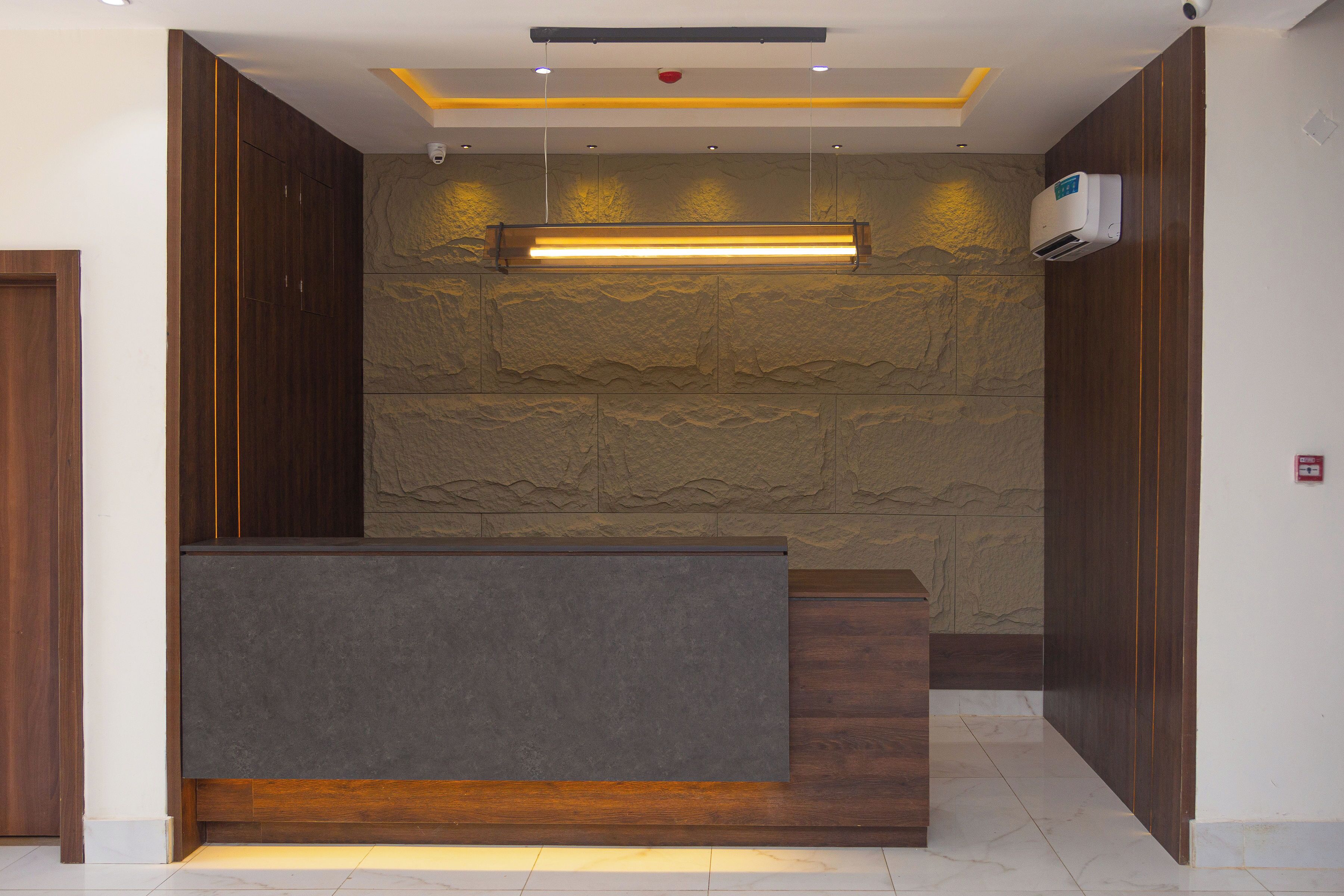 A reception area with a modern design, featuring a dark reception desk, stone-textured walls, and recessed lighting.