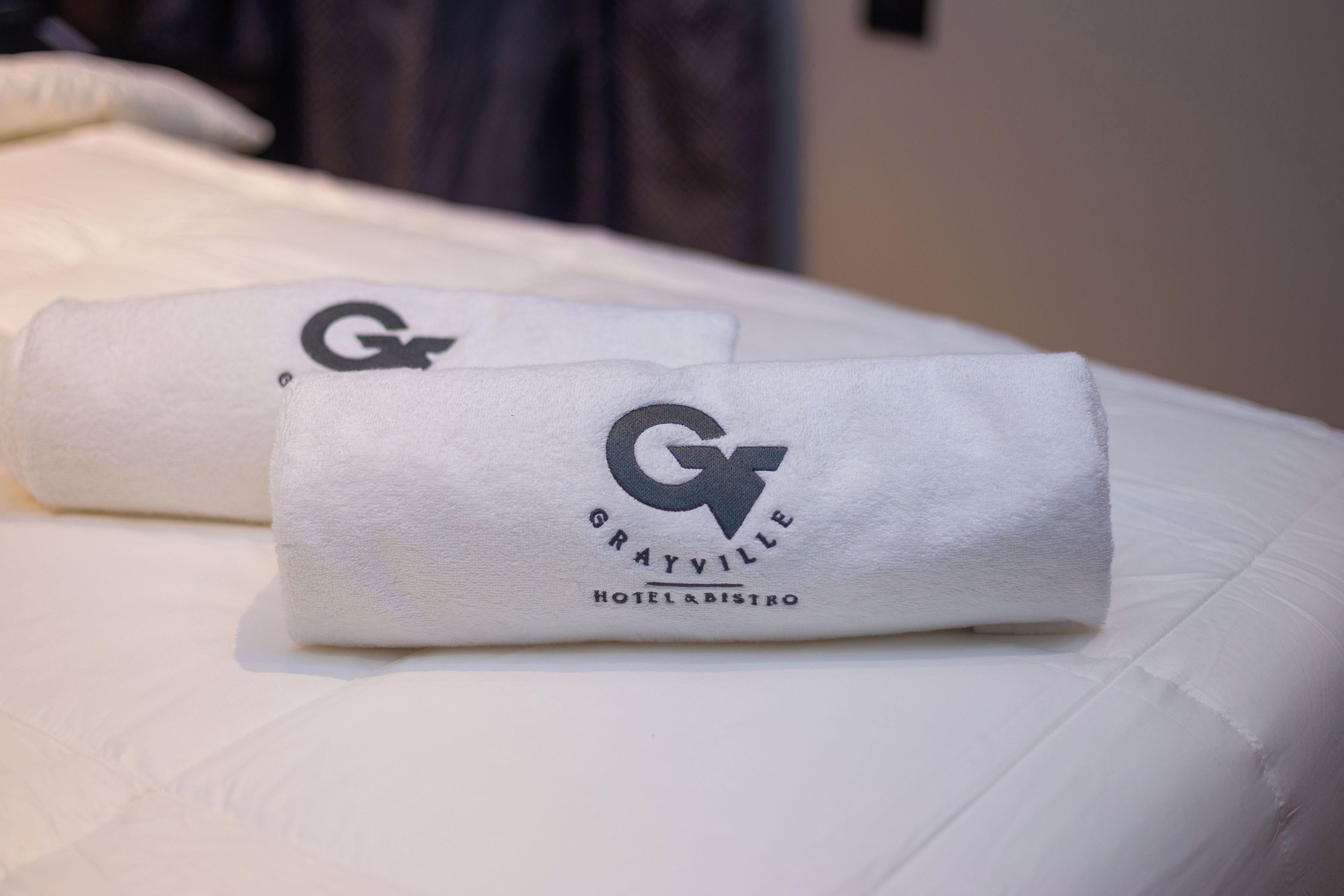 Two neatly folded towels with a logo and text on a bed.