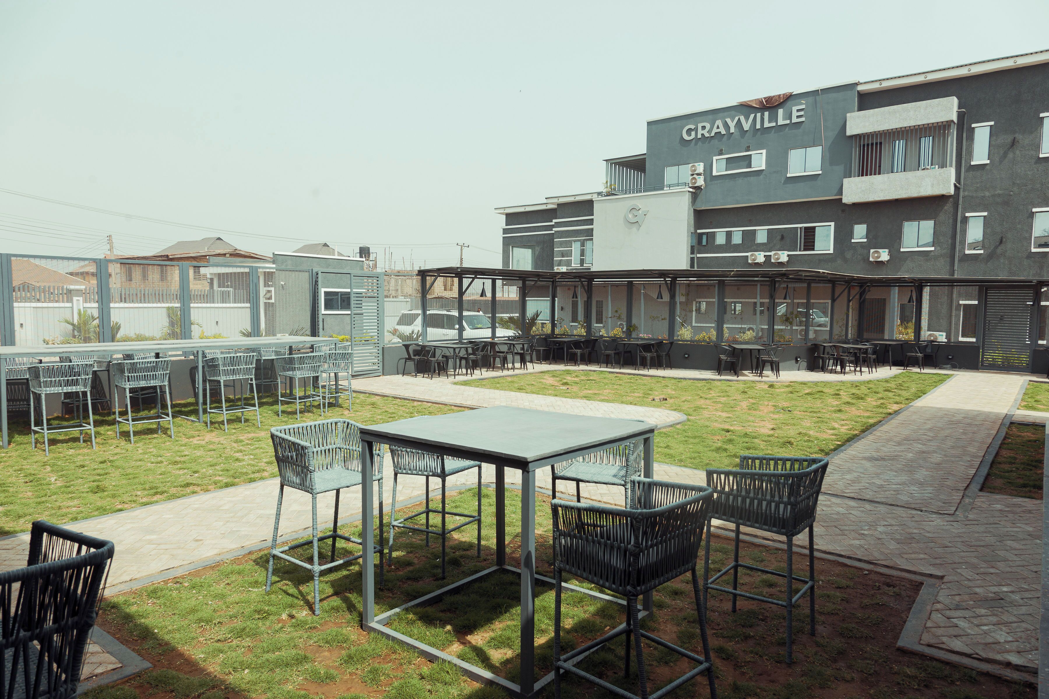 An outdoor patio area with tables and chairs, a building labeled "GRAYVILLE" in the background, and a clear sky.