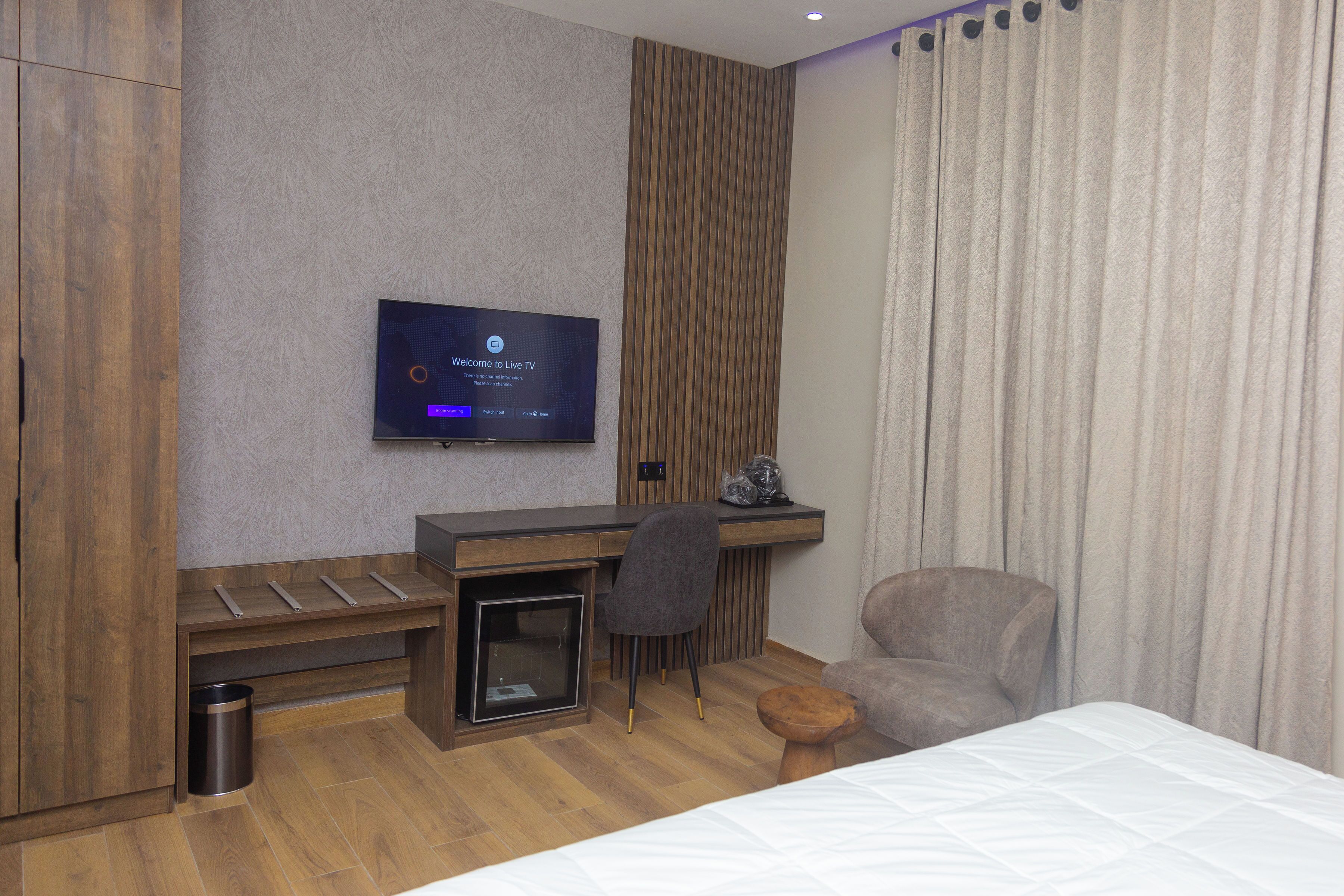 Una camera d'albergo con un letto, una scrivania con un computer, una sedia e una TV fissata al muro.