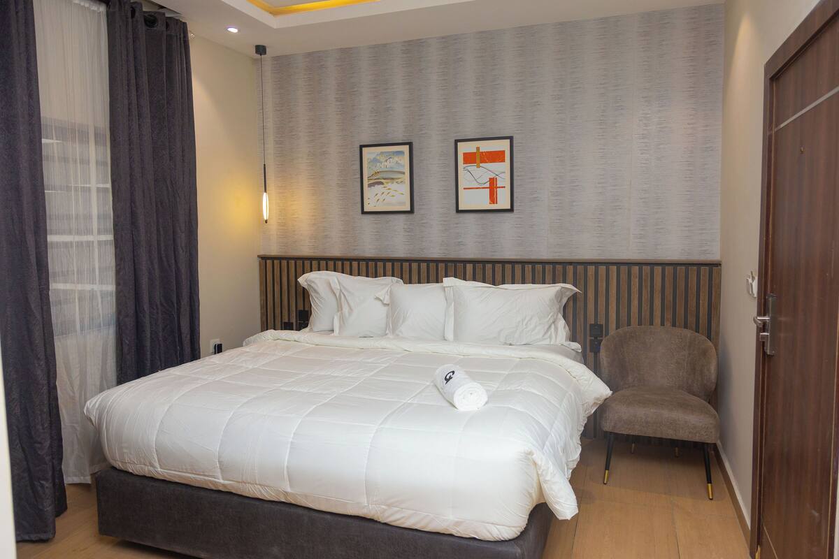 Une chambre d’hôtel avec un grand lit, une chaise, une armoire et deux tableaux encadrés au mur.