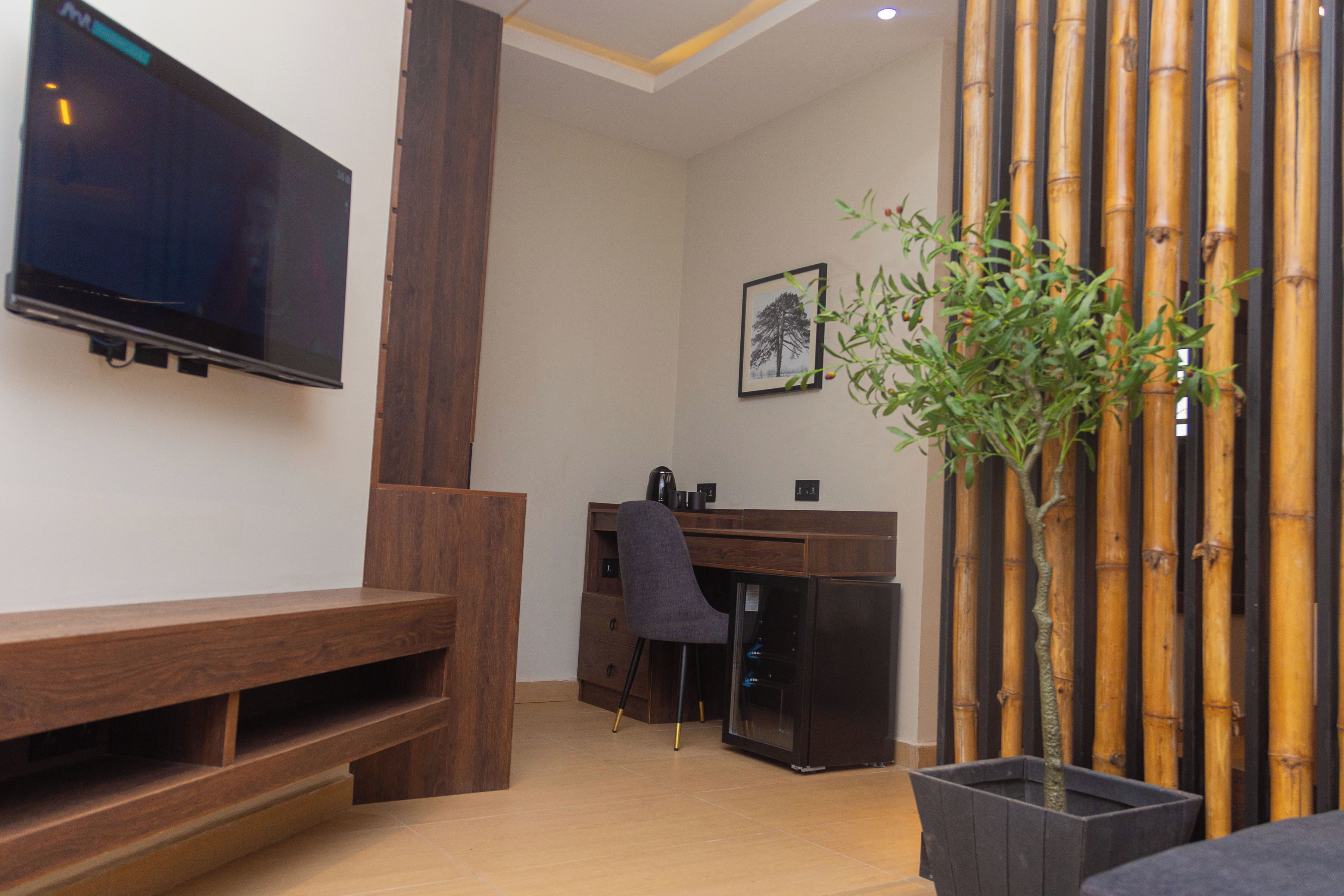 Una habitación moderna con un escritorio de madera, una silla, un televisor montado en la pared y una planta en maceta.
