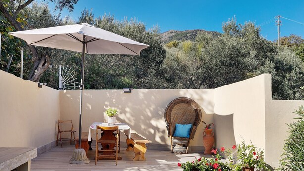 Eine Terrasse mit Tisch, Stühlen, Sonnenschirm, einem Korbstuhl und Topfpflanzen.
