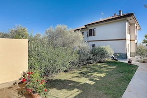 A house with a tiled roof, a garden with various plants, and a clear blue sky.