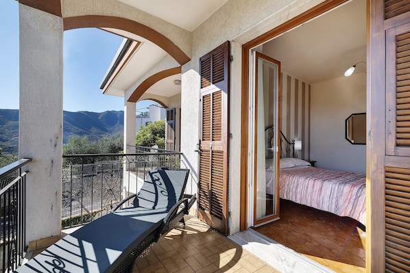 A balcony with a bed, a chair, and a view of the mountains.