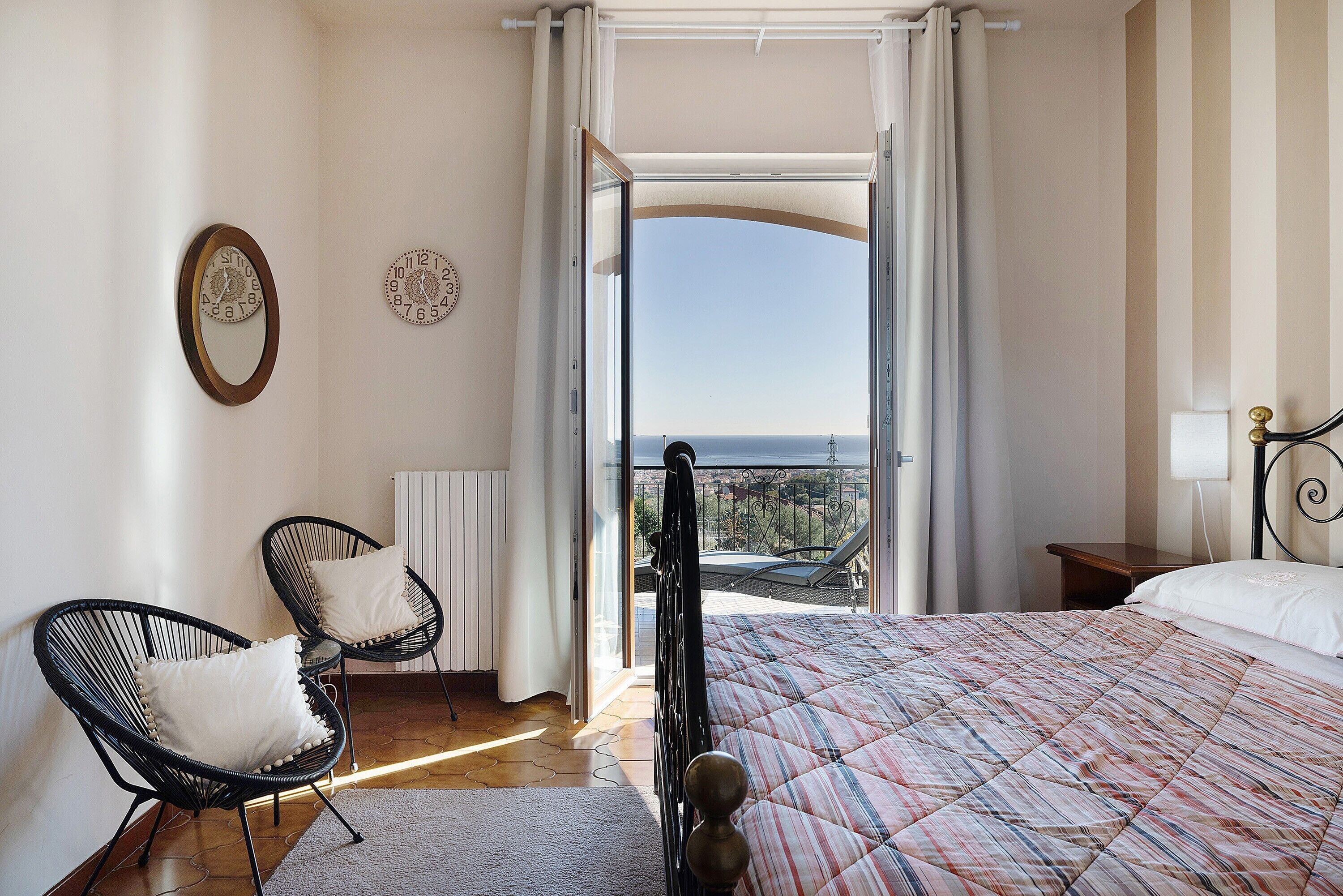 A bedroom with a bed, two chairs, a view to the outside, and a window with curtains.